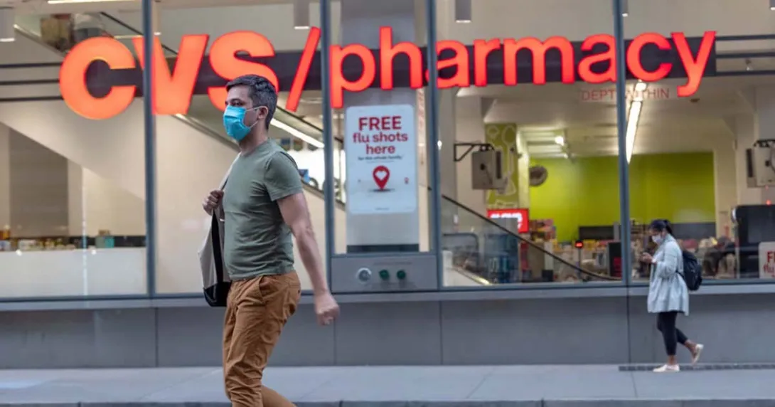 A person wearing a mask walking by a CVS pharmacy A person wearing a mask walking by a CVS pharmacy
