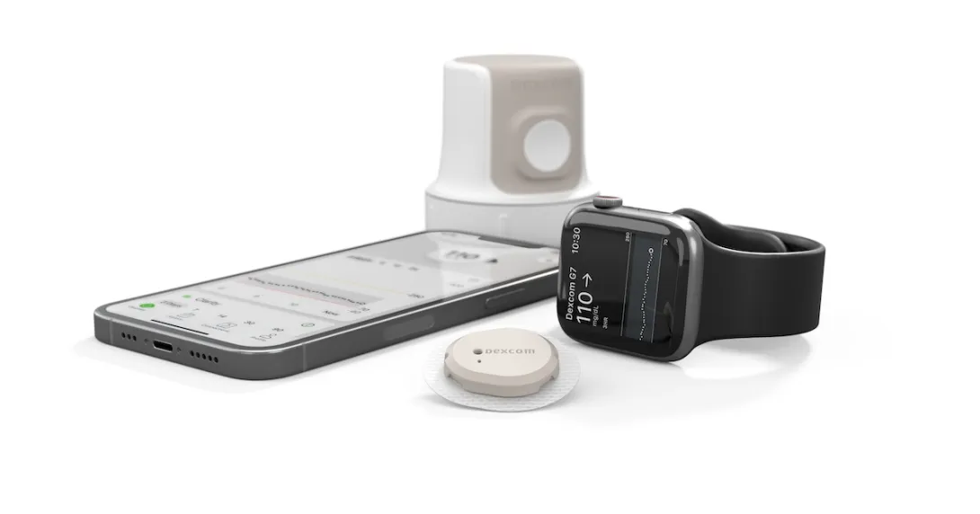 The Dexcom G7 alongside a smartphone and Apple Watch. The Dexcom G7 alongside a smartphone and Apple Watch.