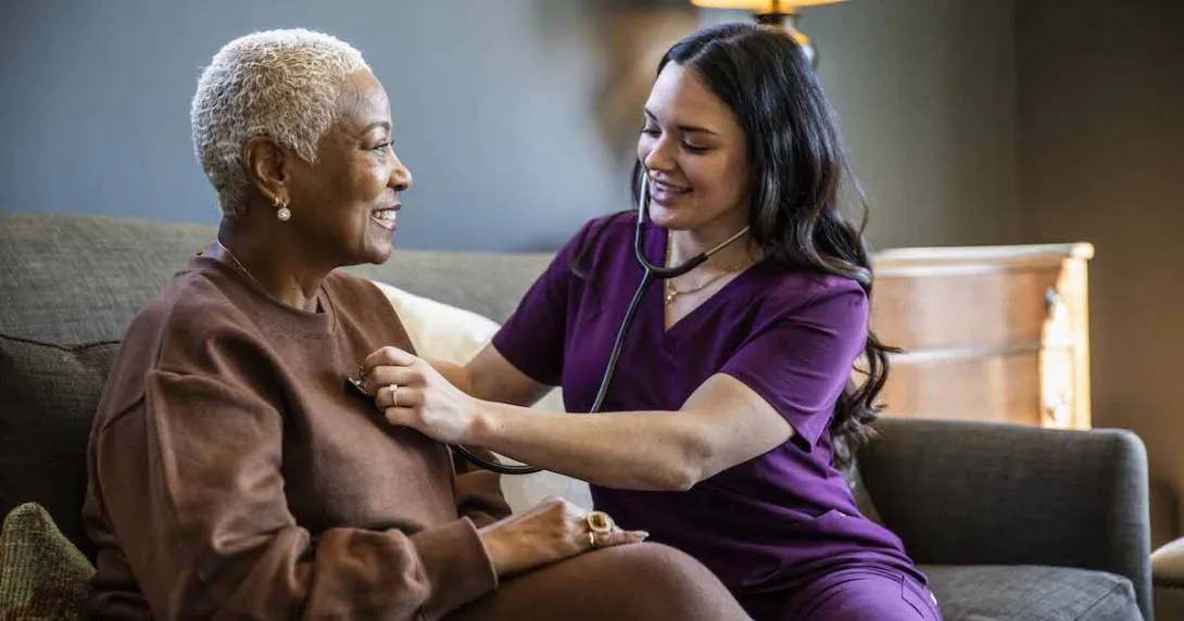 Healthcare provider sitting on a couch with a patient in their home checking their vitals. Healthcare provider sitting on a couch with a patient in their home checking their vitals.