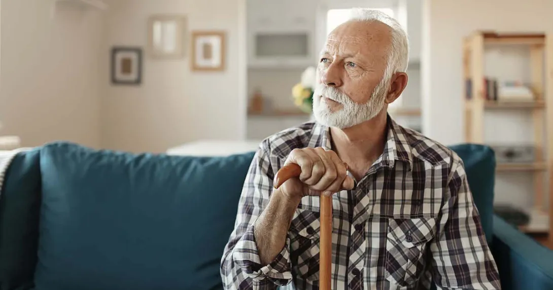 Person sitting on a couch looking away from the camera while holding a wooden cane Person sitting on a couch looking away from the camera while holding a wooden cane