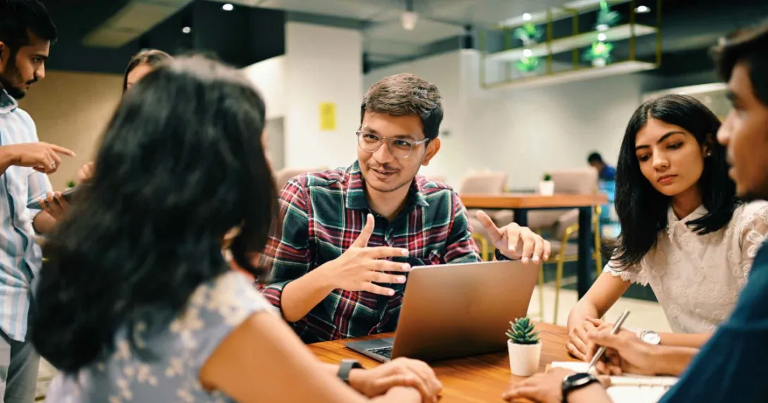 Group of individuals sitting around a table talking Group of individuals sitting around a table talking