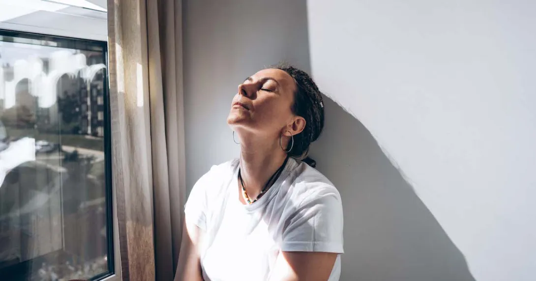 Person sitting next to a window with their eyes closed and their chin raised Person sitting next to a window with their eyes closed and their chin raised