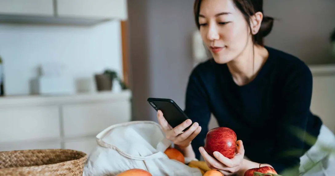 Person leaning against a counter holding an apple while looking at their phone Person leaning against a counter holding an apple while looking at their phone