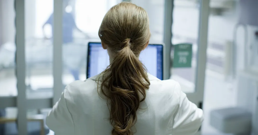 Healthcare provider with their back turned while looking at a computer Healthcare provider with their back turned while looking at a computer