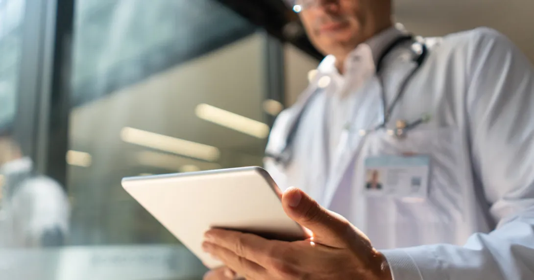Healthcare provider wearing a lab coat and stethoscope while looking at a tablet Healthcare provider wearing a lab coat and stethoscope while looking at a tablet