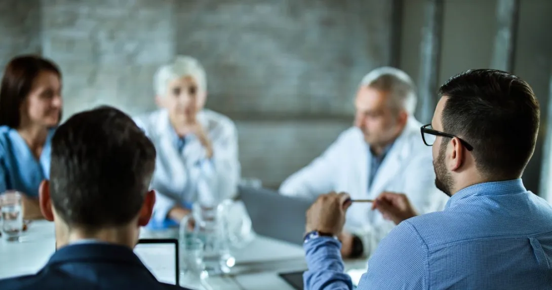 Group of people, two in lab coats, sit around table Group of people, two in lab coats, sit around table