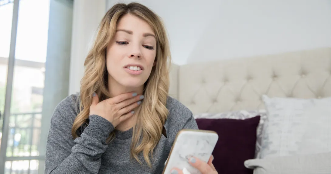 Person on a cellphone holding their throat Person on a cellphone holding their throat