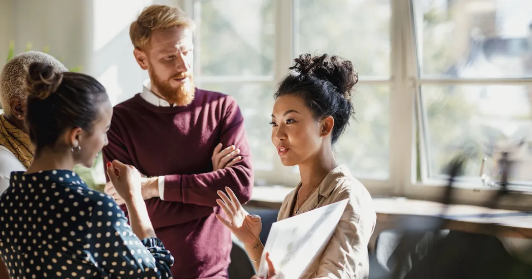 People standing in a circle with one of them holding a large piece of paper People standing in a circle with one of them holding a large piece of paper