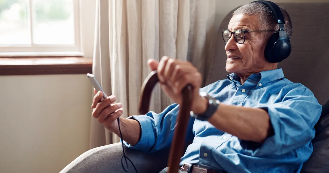 Person sitting in a chair while holding a cane and phone while wearing headphones Person sitting in a chair while holding a cane and phone while wearing headphones