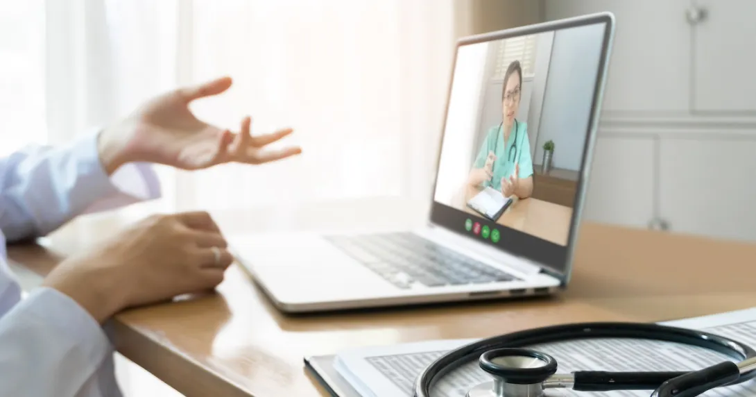Healthcare provider sitting at a desk with a computer on it and a person on the screen Healthcare provider sitting at a desk with a computer on it and a person on the screen