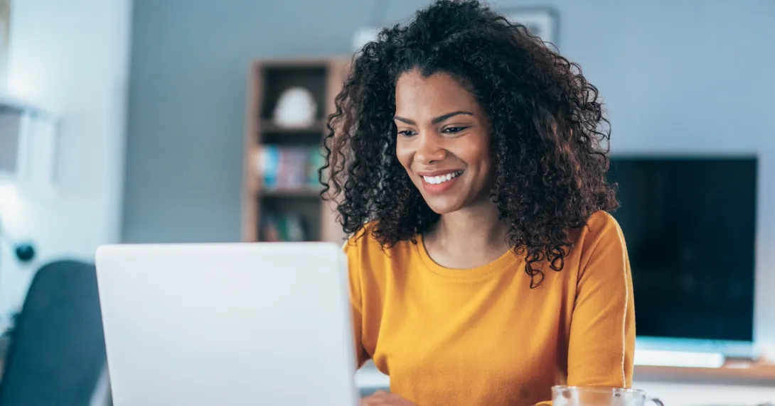 Person sitting at a table while looking at a computer and smiling Person sitting at a table while looking at a computer and smiling