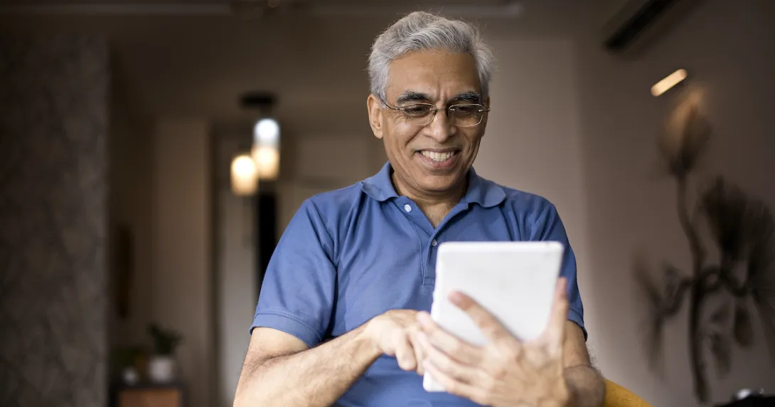 Person wearing a blue shirt and holding a tablet in the living room of a home Person wearing a blue shirt and holding a tablet in the living room of a home