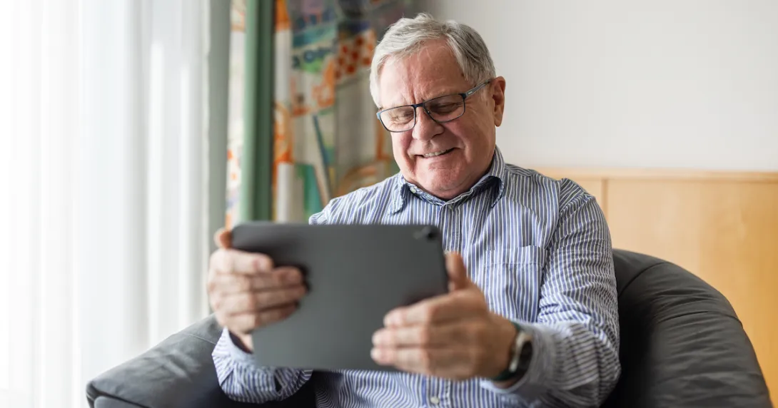 Person sitting in a chair in a home smiling while looking at a tablet Person sitting in a chair in a home smiling while looking at a tablet