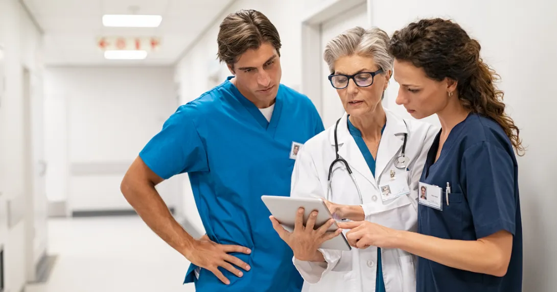 Healthcare providers standing in the hallway of a hospital looking at a tablet Healthcare providers standing in the hallway of a hospital looking at a tablet