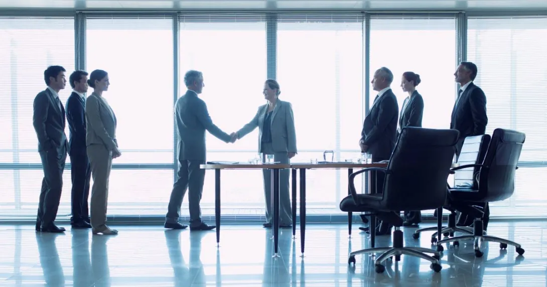 Group of three people on left, two people shaking hands in middle, three people standing behind office chairs on right Group of three people on left, two people shaking hands in middle, three people standing behind office chairs on right