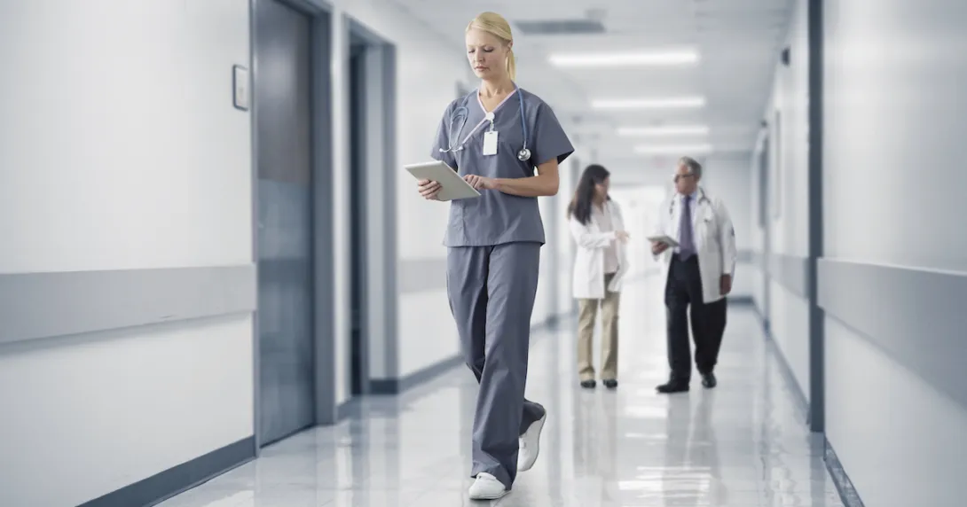 Healthcare provider walking through a hallway with two other healthcare providers standing behind them Healthcare provider walking through a hallway with two other healthcare providers standing behind them