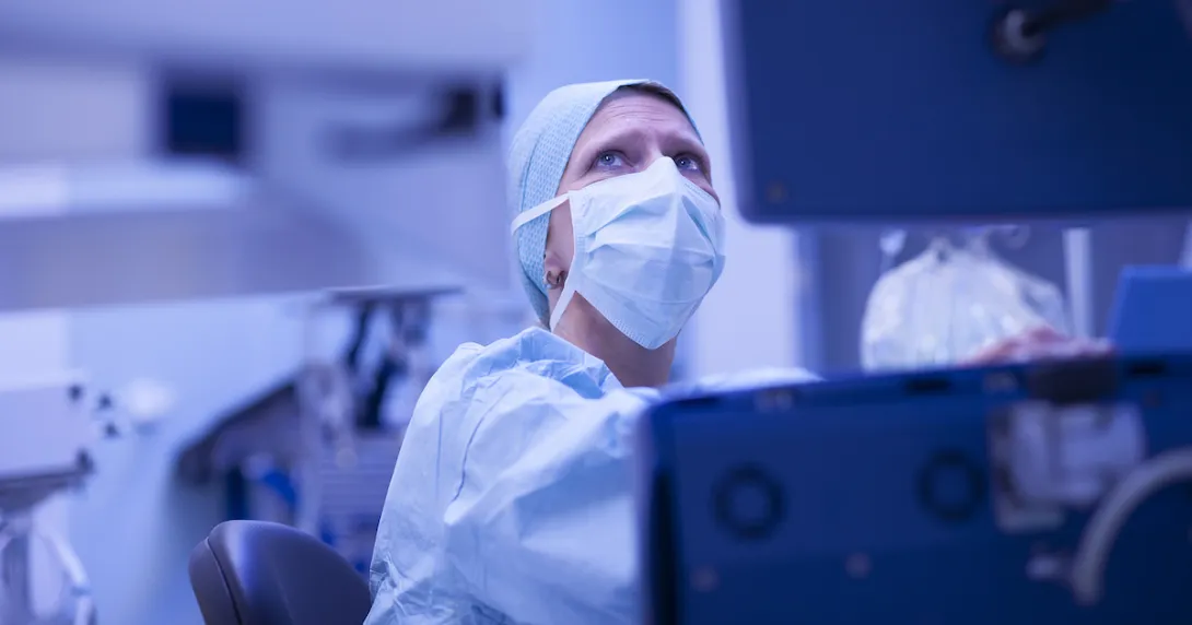 Healthcare provider wearing scrubs and a face mask while looking at a computer screen Healthcare provider wearing scrubs and a face mask while looking at a computer screen