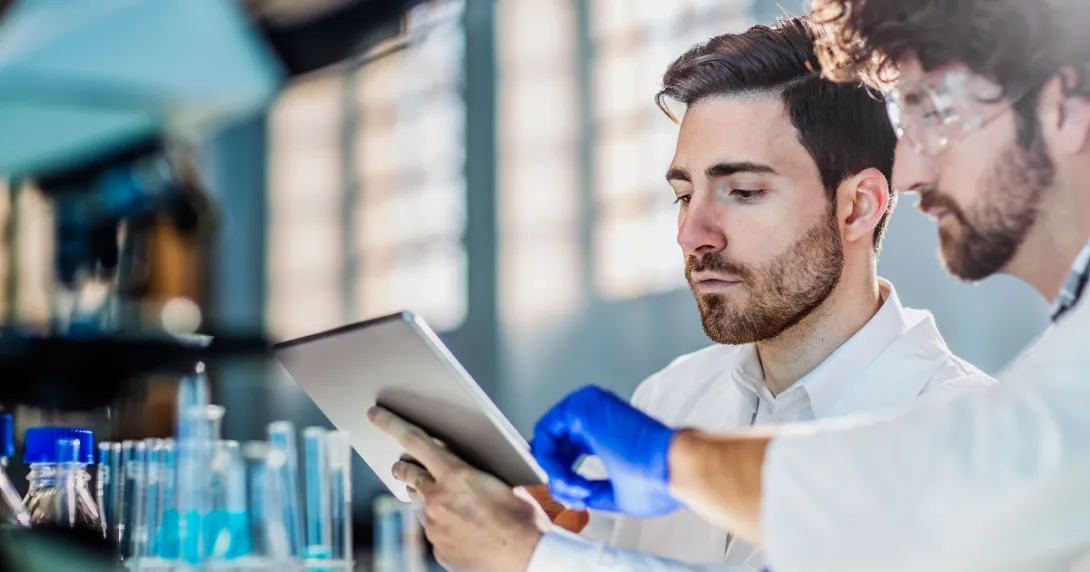 Two scientists in a laboratory setting looking at a tablet while surrounded by beakers Two scientists in a laboratory setting looking at a tablet while surrounded by beakers