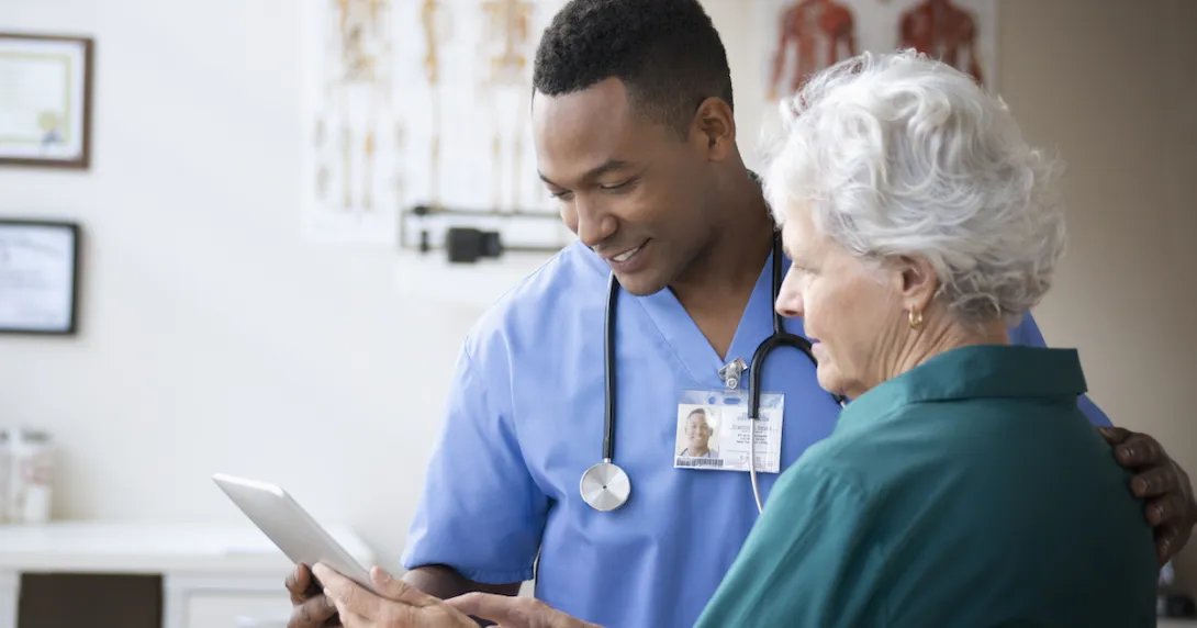 Healthcare professional standing next to a patient while holding a tablet Healthcare professional standing next to a patient while holding a tablet