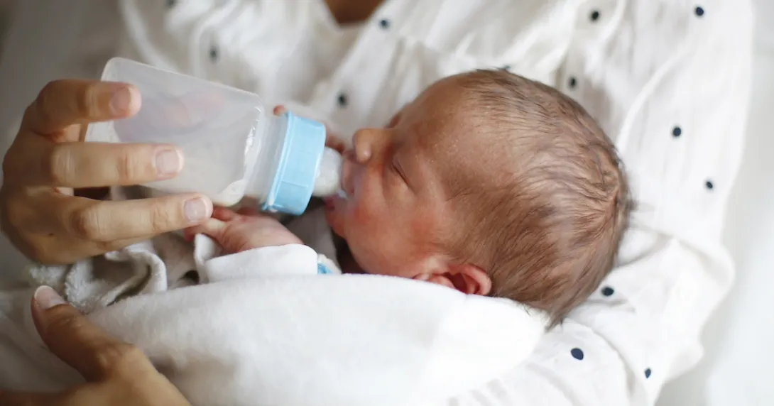 Person holding another small person while feeding them with a bottle Person holding another small person while feeding them with a bottle