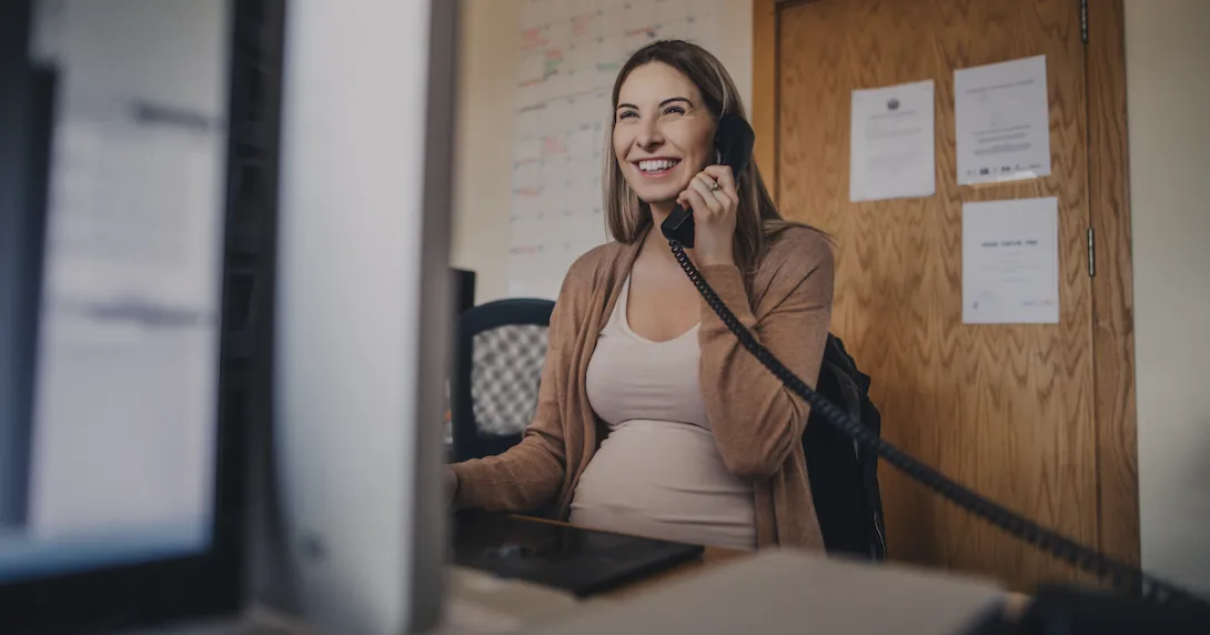Pregnant person sitting at a desk talking on the phone while looking at a computer Pregnant person sitting at a desk talking on the phone while looking at a computer