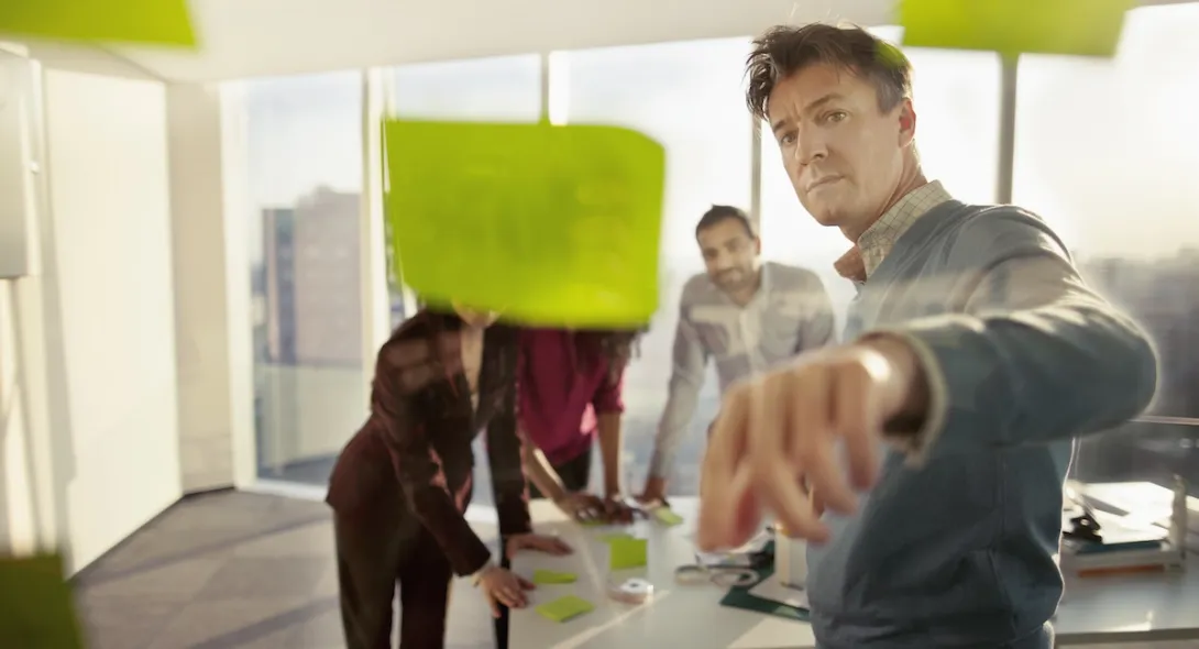 People standing in a board room looking at post it notes on a wall