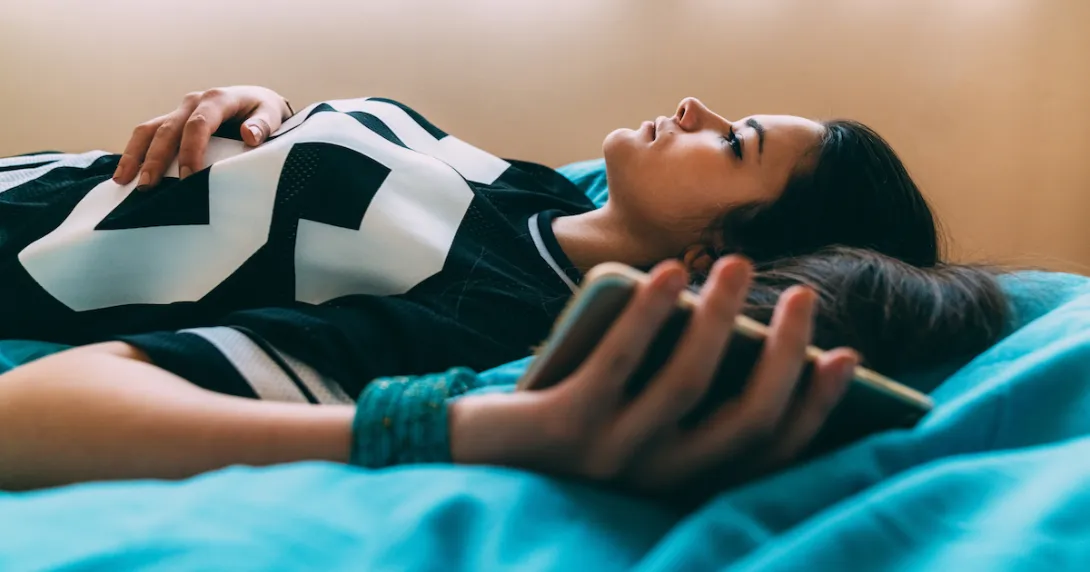 Person lying on a bed looking up at the ceiling while holding onto a cellphone
