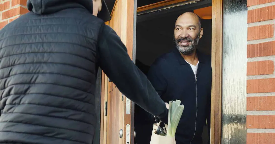 Person answering their front door and getting a delivery from another person Person answering their front door and getting a delivery from another person