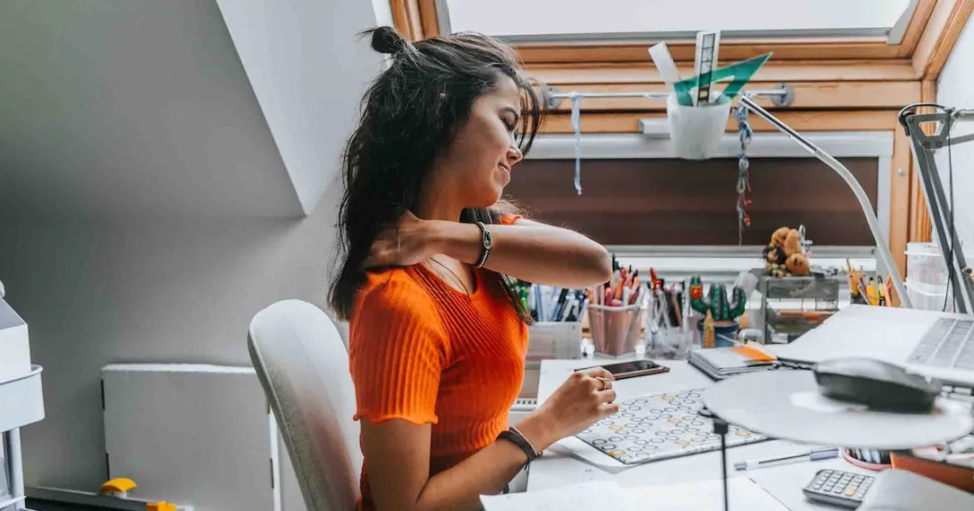 Person rubbing their neck while sitting at a desk