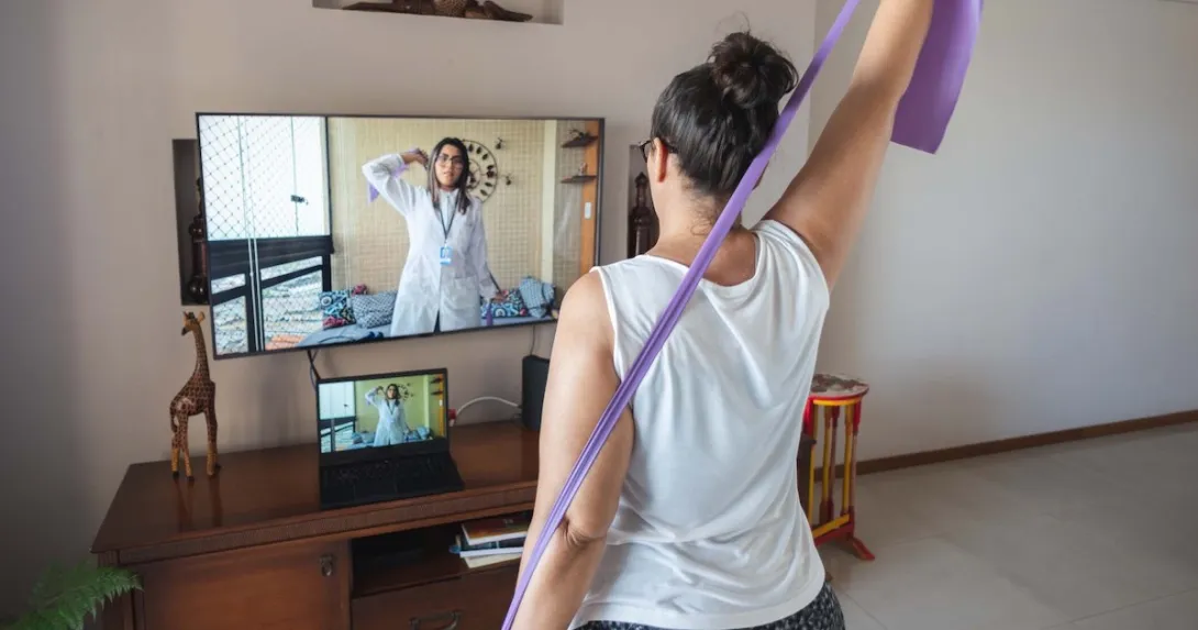 A woman doing exercises guided by a physical therapist on her screen A woman doing exercises guided by a physical therapist on her screen