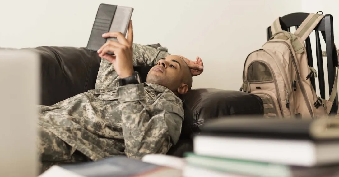 Soldier using digital tablet on sofa near books Soldier using digital tablet on sofa near books
