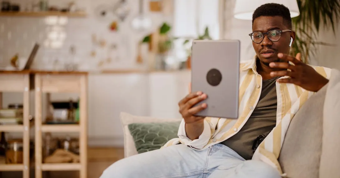 Person sitting on the couch in a home while holding up a tablet in front of them Person sitting on the couch in a home while holding up a tablet in front of them