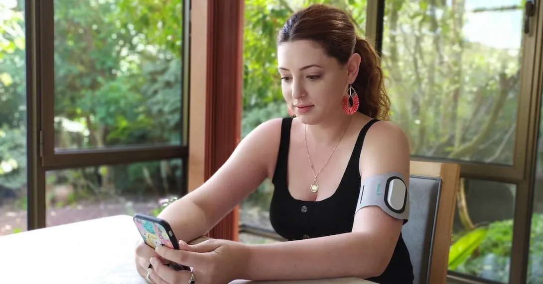 A person wearing an armband with the Theranica device while holding a smartphone. A person wearing an armband with the Theranica device while holding a smartphone.