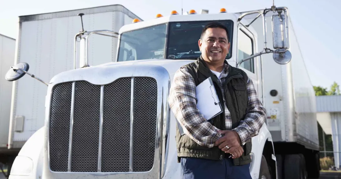 Truck driver standing in front of a semi-truck while holding a clipboard Truck driver standing in front of a semi-truck while holding a clipboard