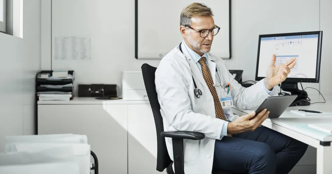 A doctor using a tablet at his desk in a clinic. A doctor using a tablet at his desk in a clinic.