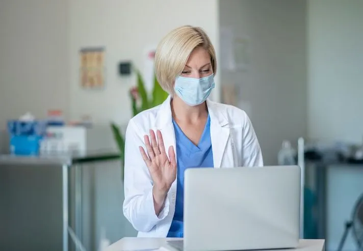 A doctor wearing a mask talking to a patient via telehealth A doctor wearing a mask talking to a patient via telehealth