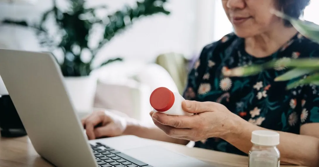 A woman holding a pill bottle and using a laptop. A woman holding a pill bottle and using a laptop.