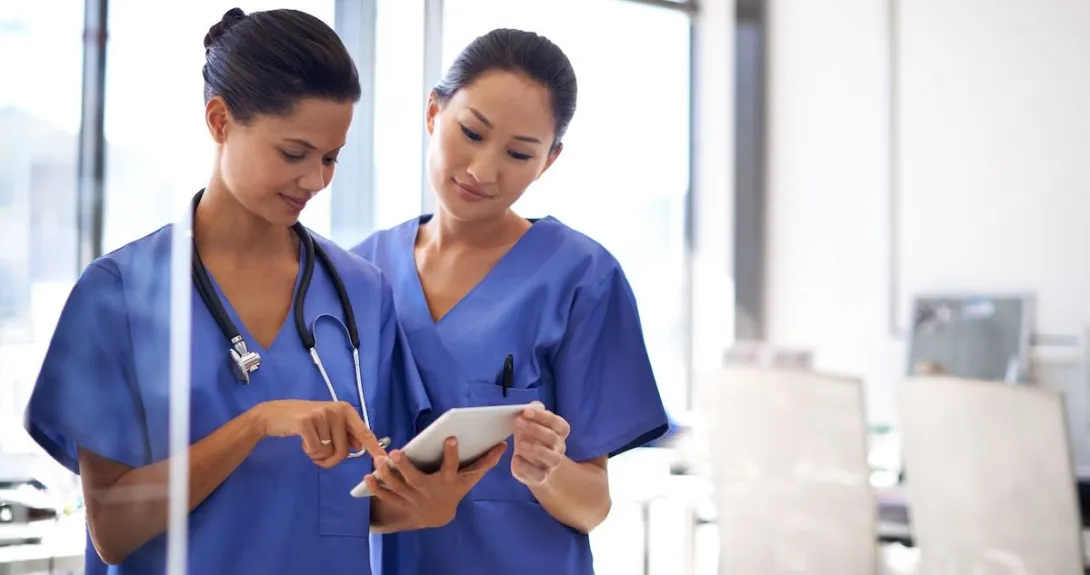 Two nurses using a tablet to review medical records. Two nurses using a tablet to review medical records.