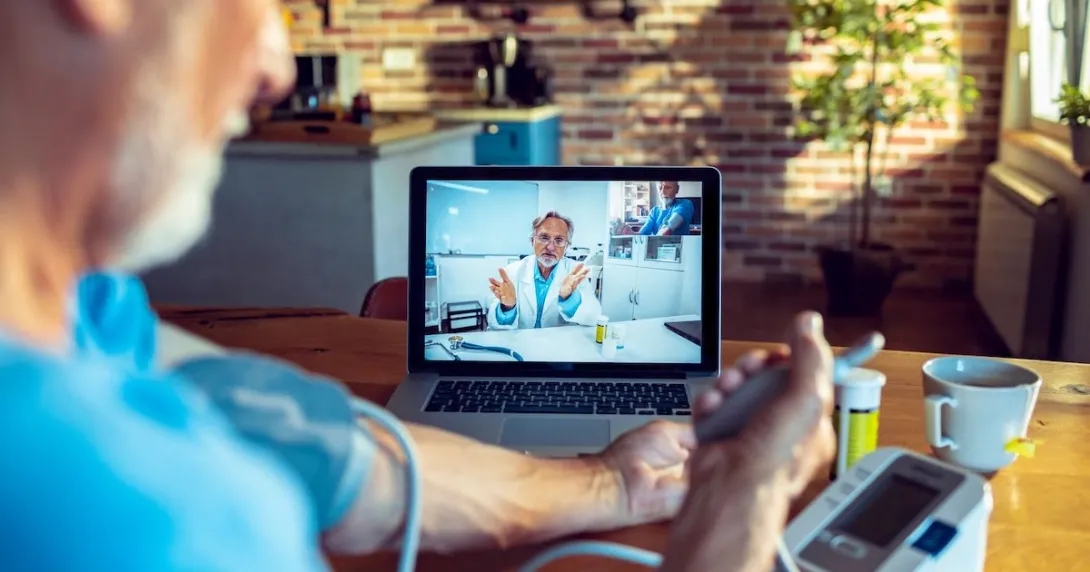 An older man talking with a provider on his laptop while checking his blood pressure