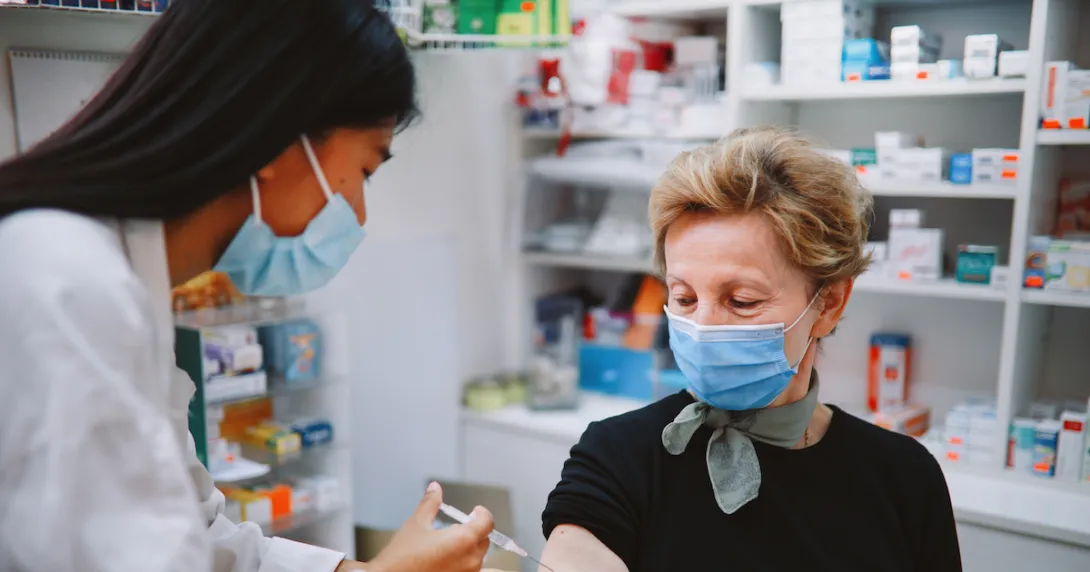An older woman getting a shot from a pharmacist