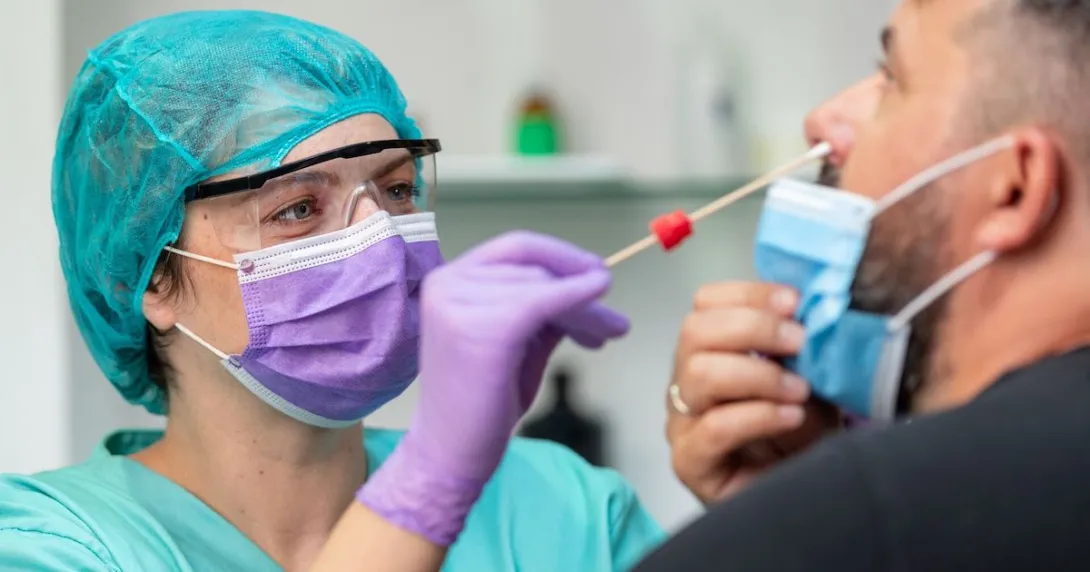 Female doctor in protective workwear taking nose swab test from middle aged man wearing protective face mask Female doctor in protective workwear taking nose swab test from middle aged man wearing protective face mask