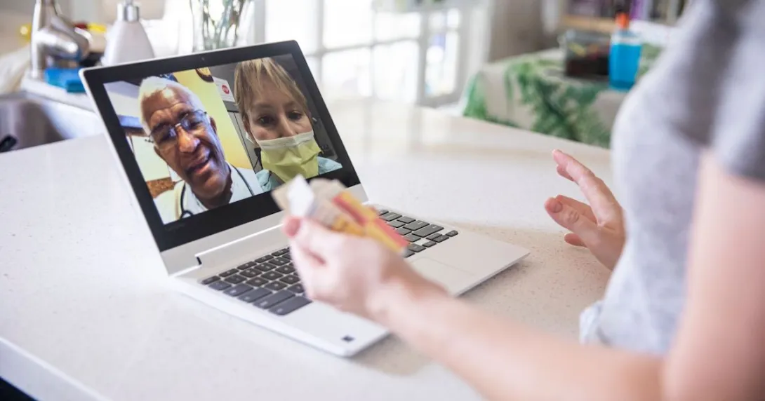 A close up of a woman holding a prescription while talking to two providers on her laptop A close up of a woman holding a prescription while talking to two providers on her laptop