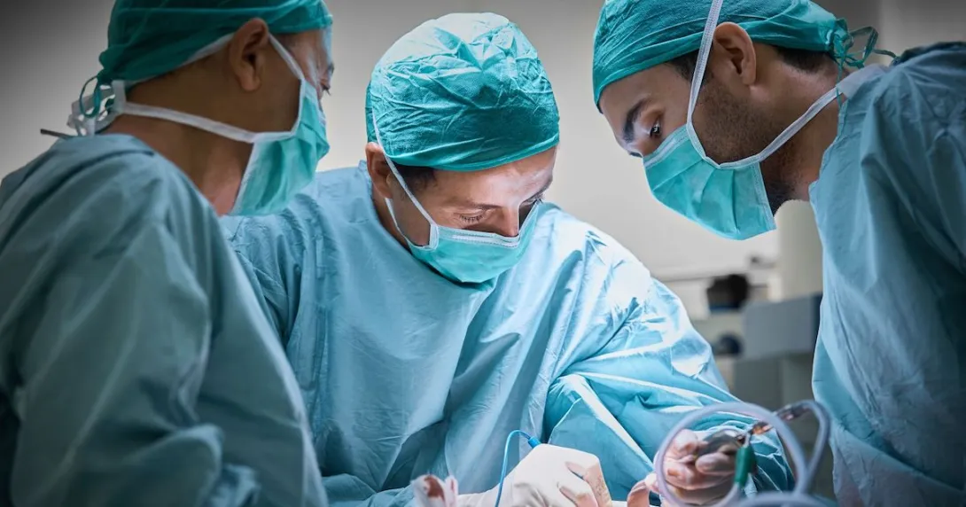 Three healthcare providers in scrubs performing surgery on a patient Three healthcare providers in scrubs performing surgery on a patient