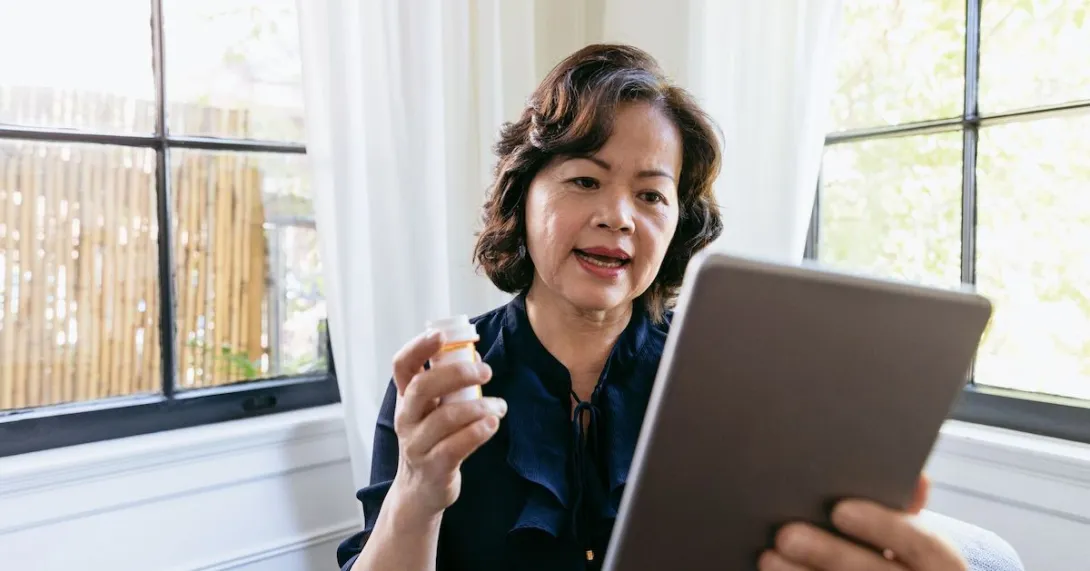 Person holding a tablet in one hand and a prescription bottle in the other Person holding a tablet in one hand and a prescription bottle in the other