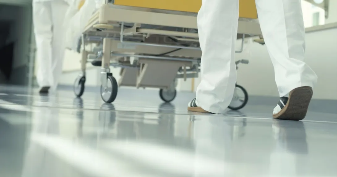 The legs of healthcare professionals pushing a hospital bed through a hallway The legs of healthcare professionals pushing a hospital bed through a hallway