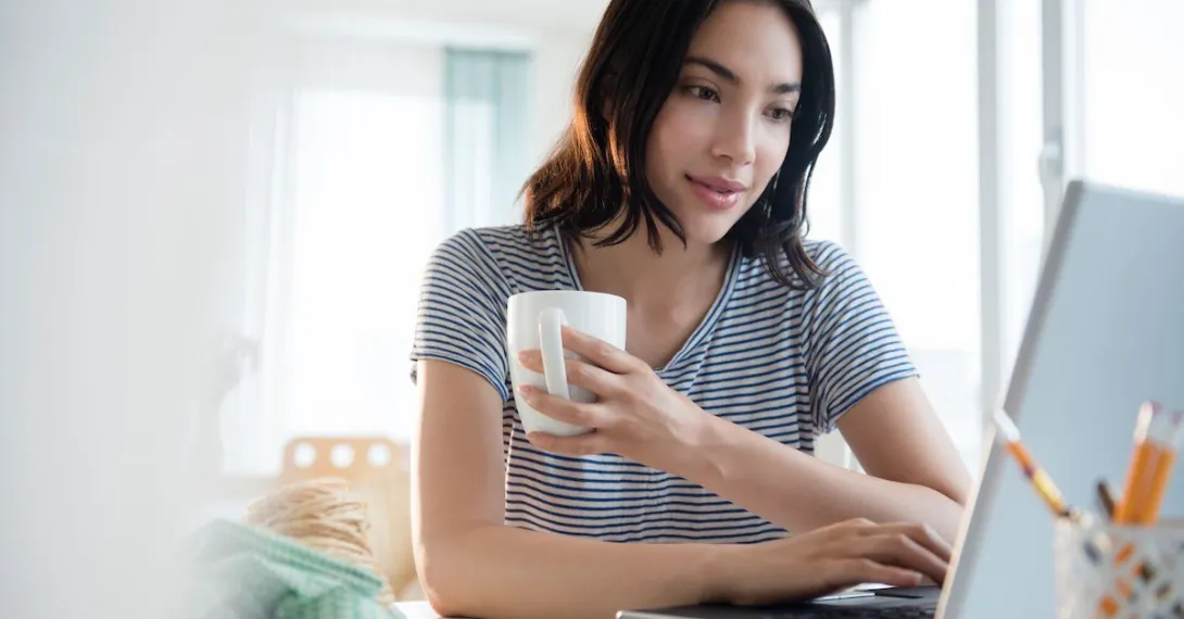 Person sitting at a computer while holding a cup of coffee Person sitting at a computer while holding a cup of coffee