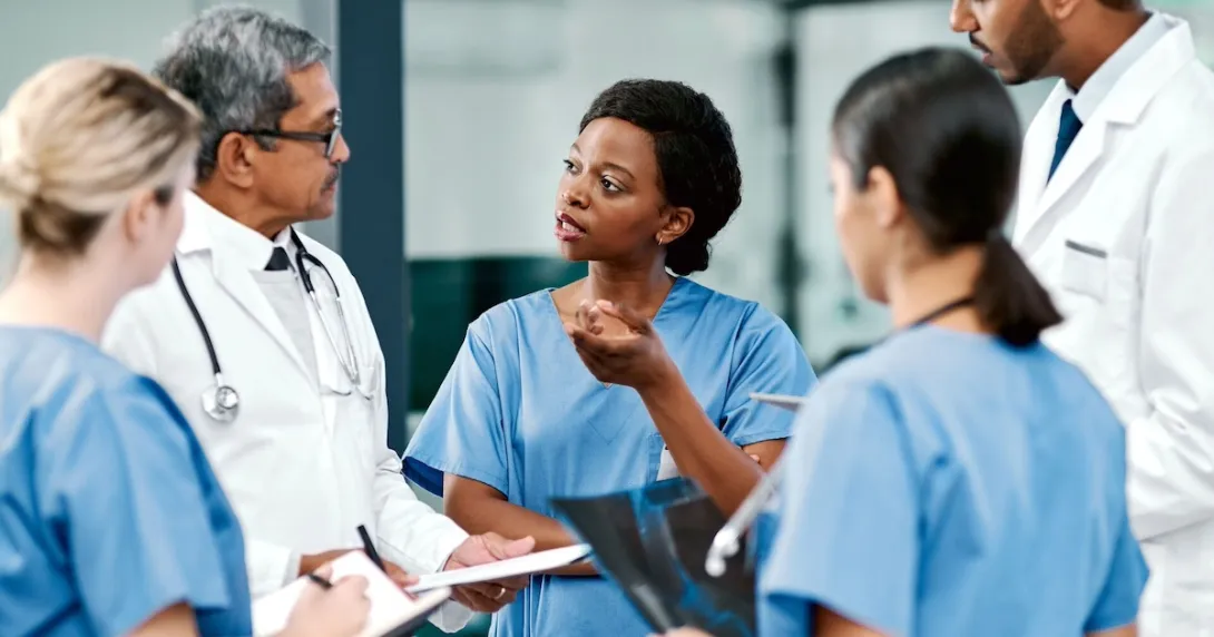 Five healthcare providers standing in a circle, talking to each other Five healthcare providers standing in a circle, talking to each other