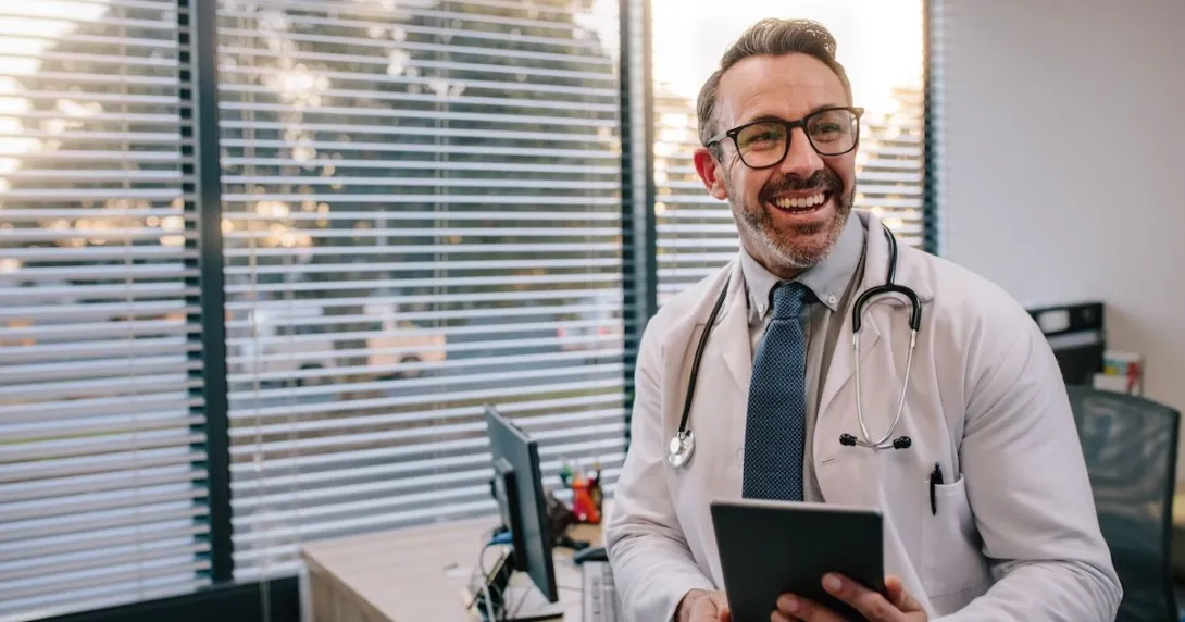 Doctor leaning against a desk while holding a tablet Doctor leaning against a desk while holding a tablet
