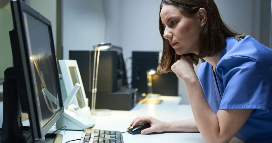 Healthcare provider sitting at a desk looking at a screen with their hand on the mouse Healthcare provider sitting at a desk looking at a screen with their hand on the mouse