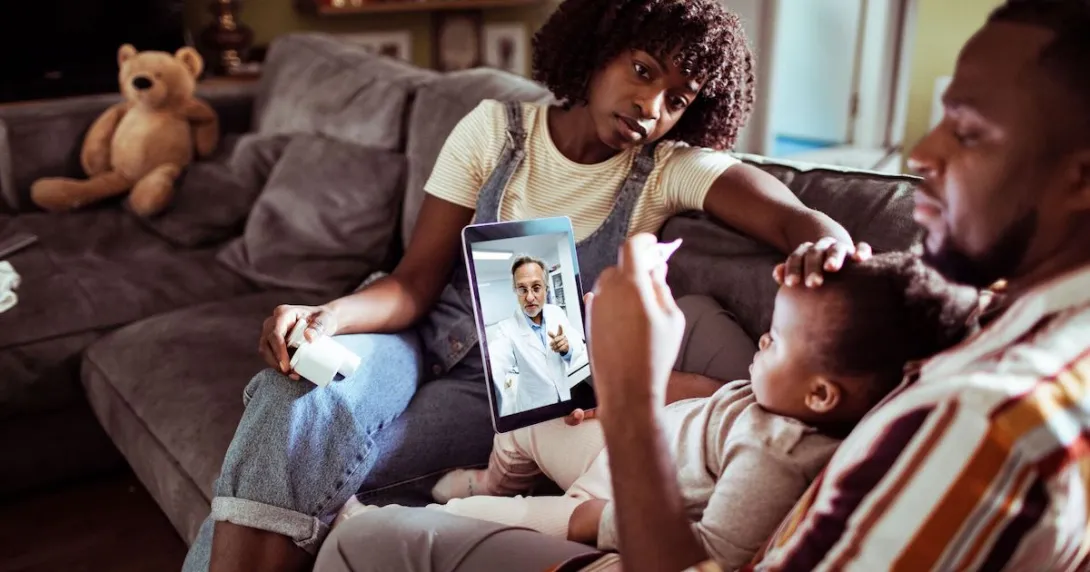 Three people sitting on a couch looking at a computer with a healthcare provider on the screen Three people sitting on a couch looking at a computer with a healthcare provider on the screen